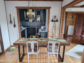 A dining area with a wooden table, white chairs, and a chandelier. - 4 Star Holiday Home in Farosund (Fårösund)