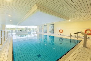 An indoor swimming pool with clear water, a tiled deck, and a lifebuoy on the wall. - 2 Raum Appartement im IFA Fehmarn mit Balkon (Fehmarn)