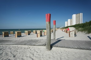 A beach with beach chairs and umbrellas, a wooden walkway, and tall buildings in the background. - 2 Raum Appartement im IFA Fehmarn mit Balkon (Fehmarn)