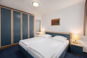 A hotel room with a double bed, two bedside tables with lamps, a wardrobe, a mirror, and a painting on the wall. - 2 Raum Appartement im IFA Fehmarn mit Balkon (Fehmarn)