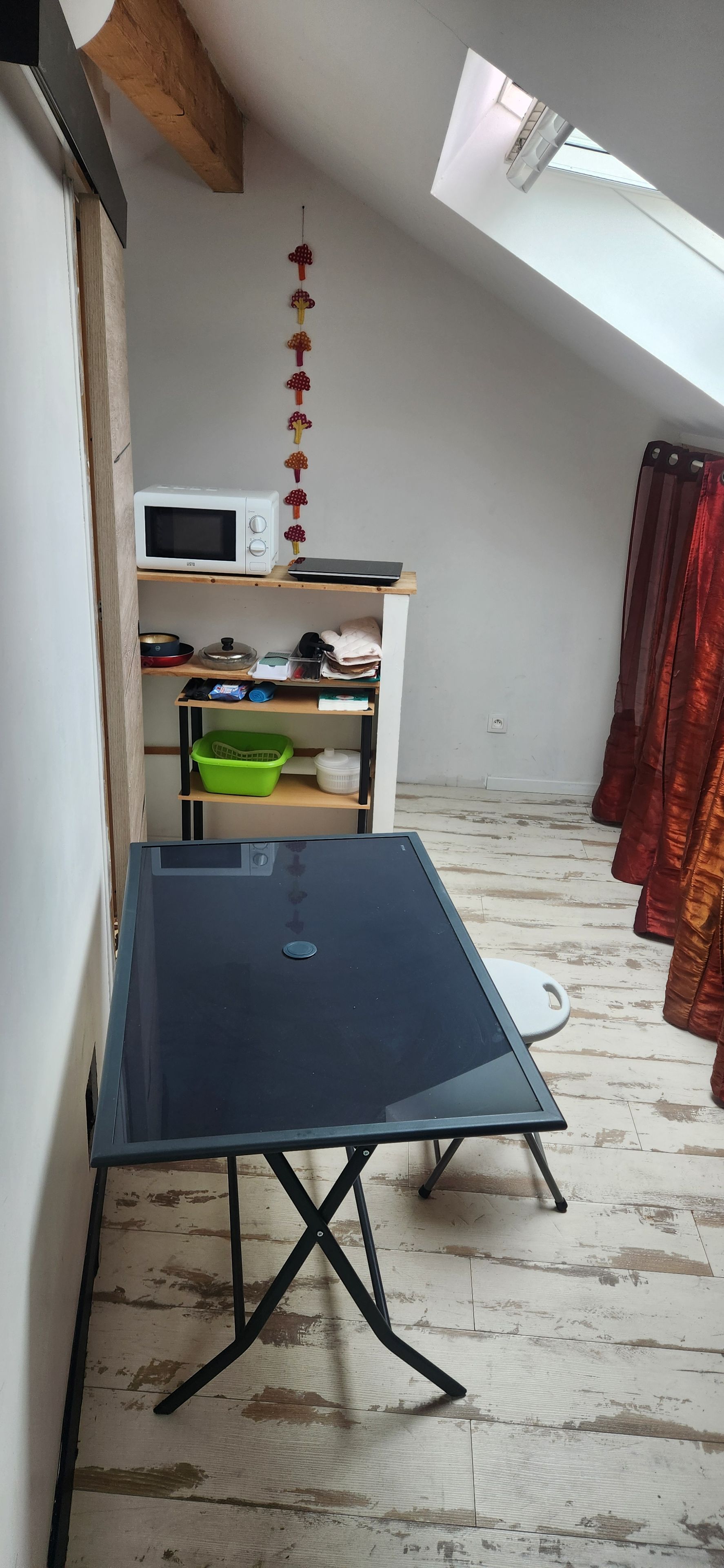 Una habitación con una mesa negra, un estante blanco con varios objetos y una cortina roja.