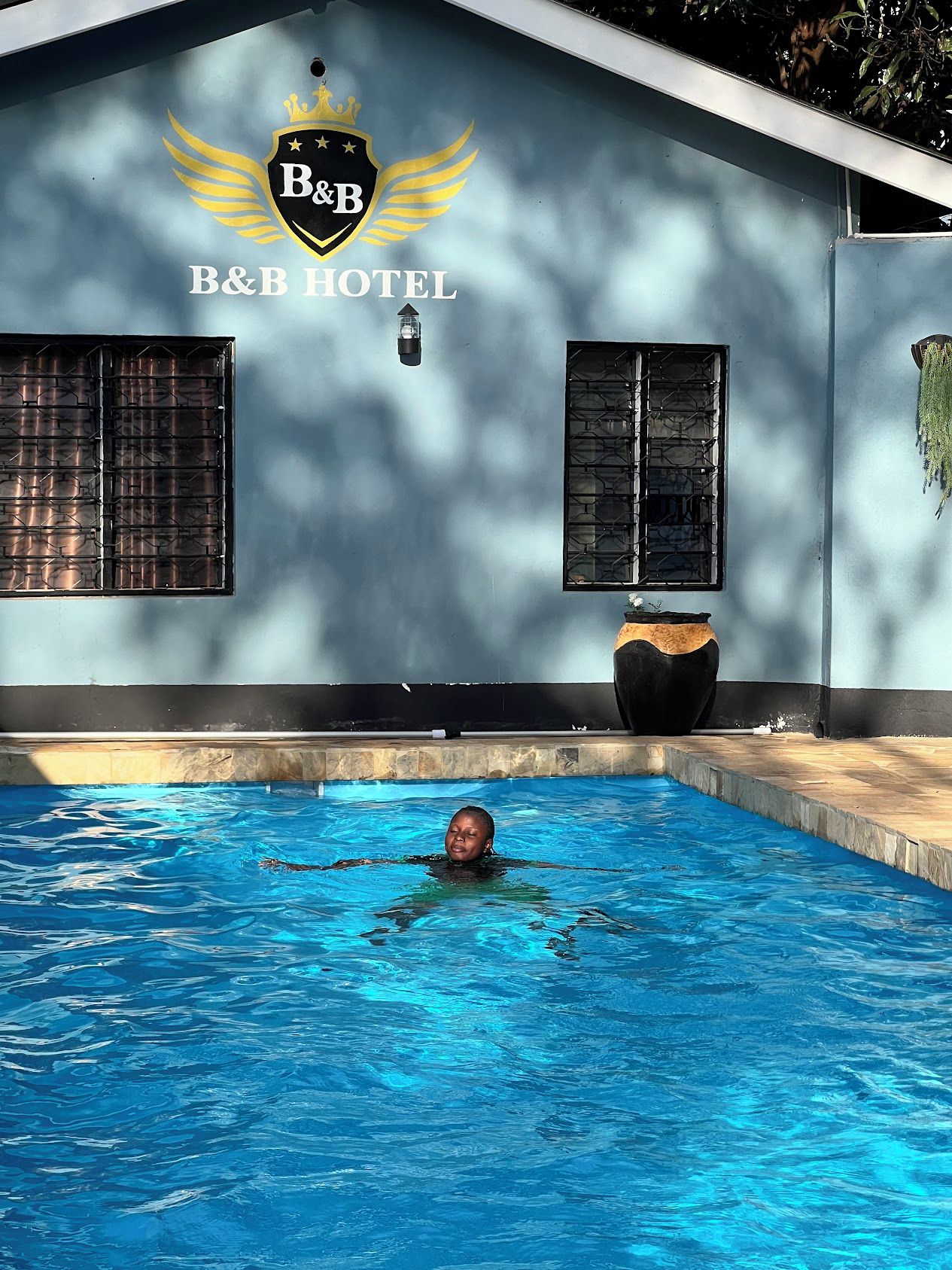 A swimming pool with a person in it, a B&B hotel sign, and a large planter.