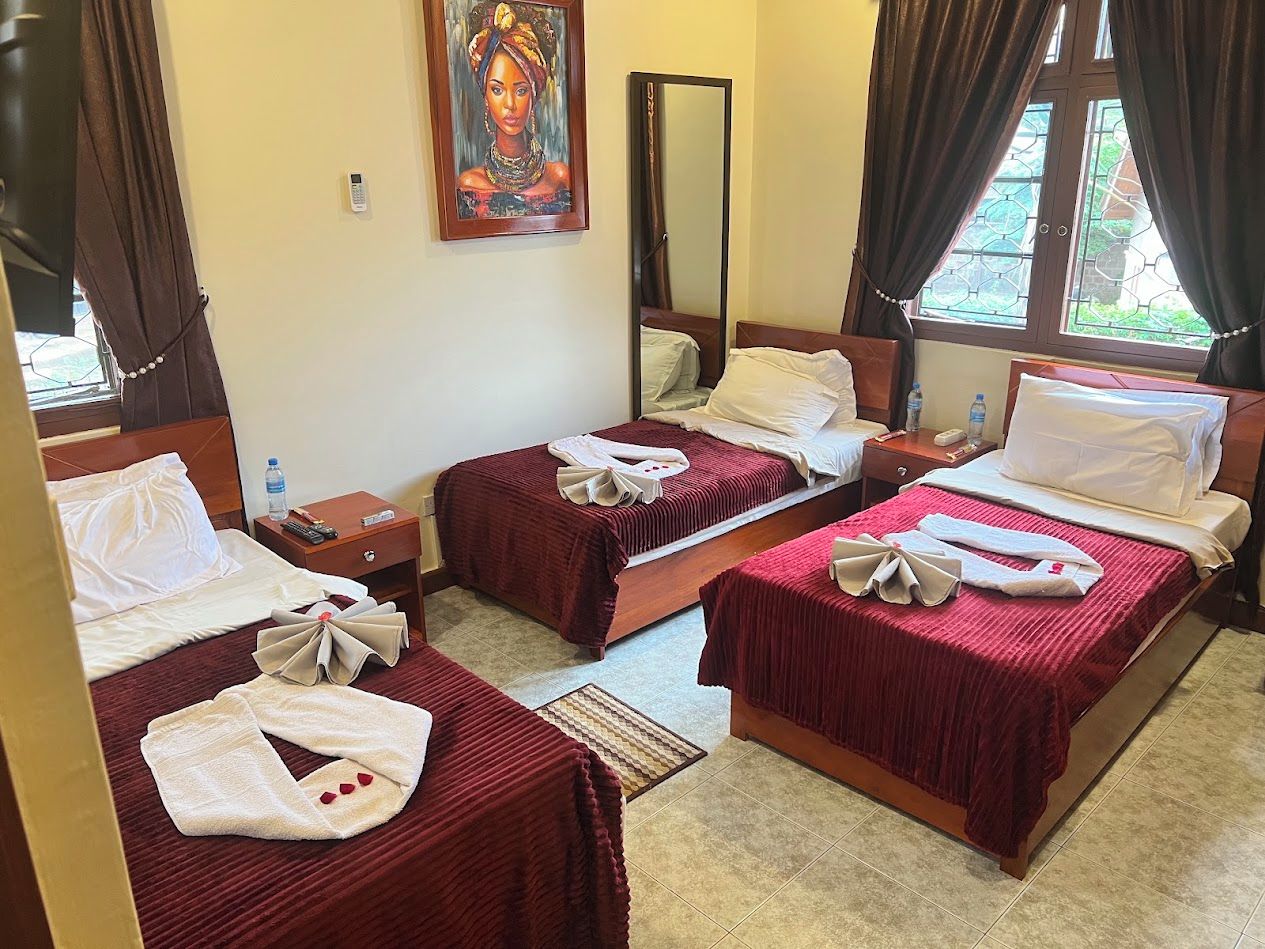 A hotel room with two beds, a painting on the wall, a mirror, and a window with curtains.