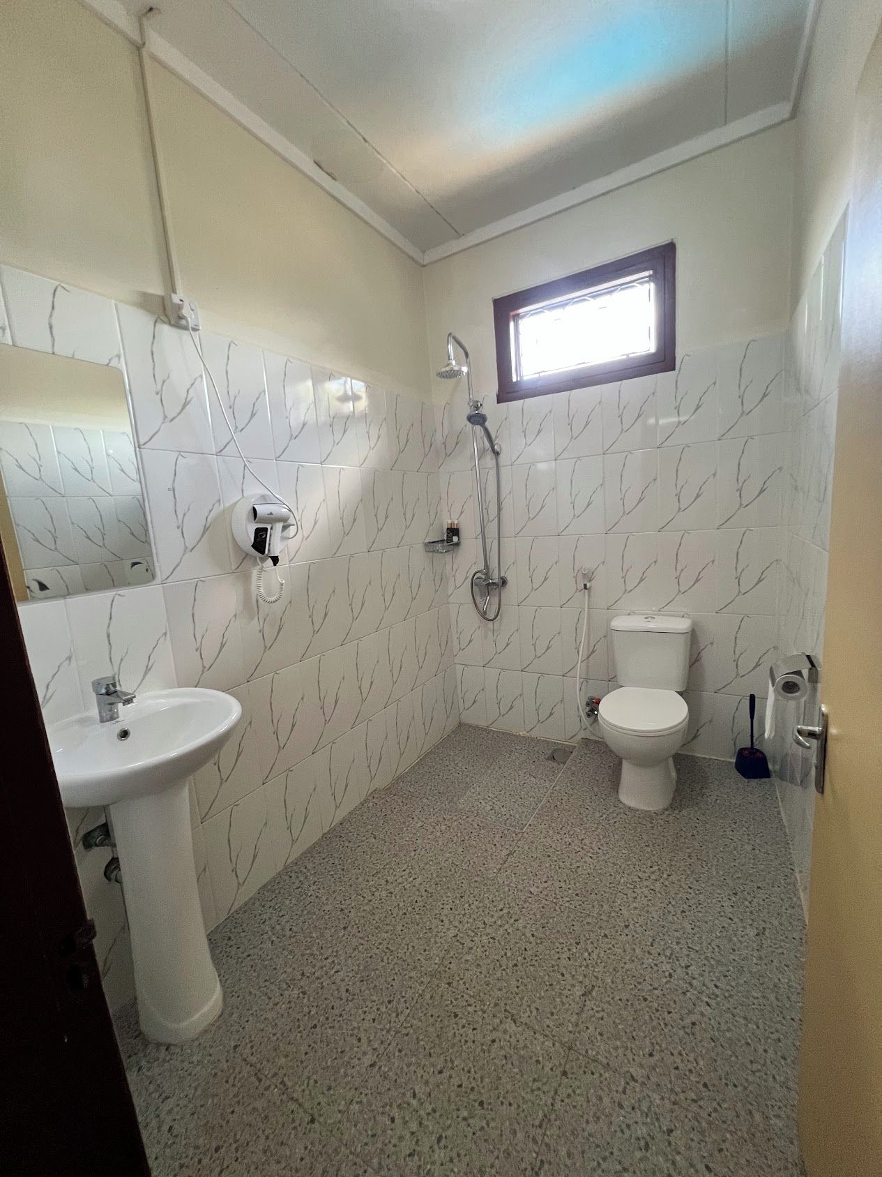 A bathroom with a white marble tile pattern, a sink, a toilet, and a shower.