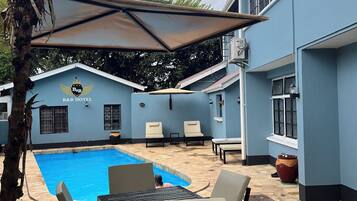 A pool area with lounge chairs and a table, a palm tree, and a building with a B&B logo.