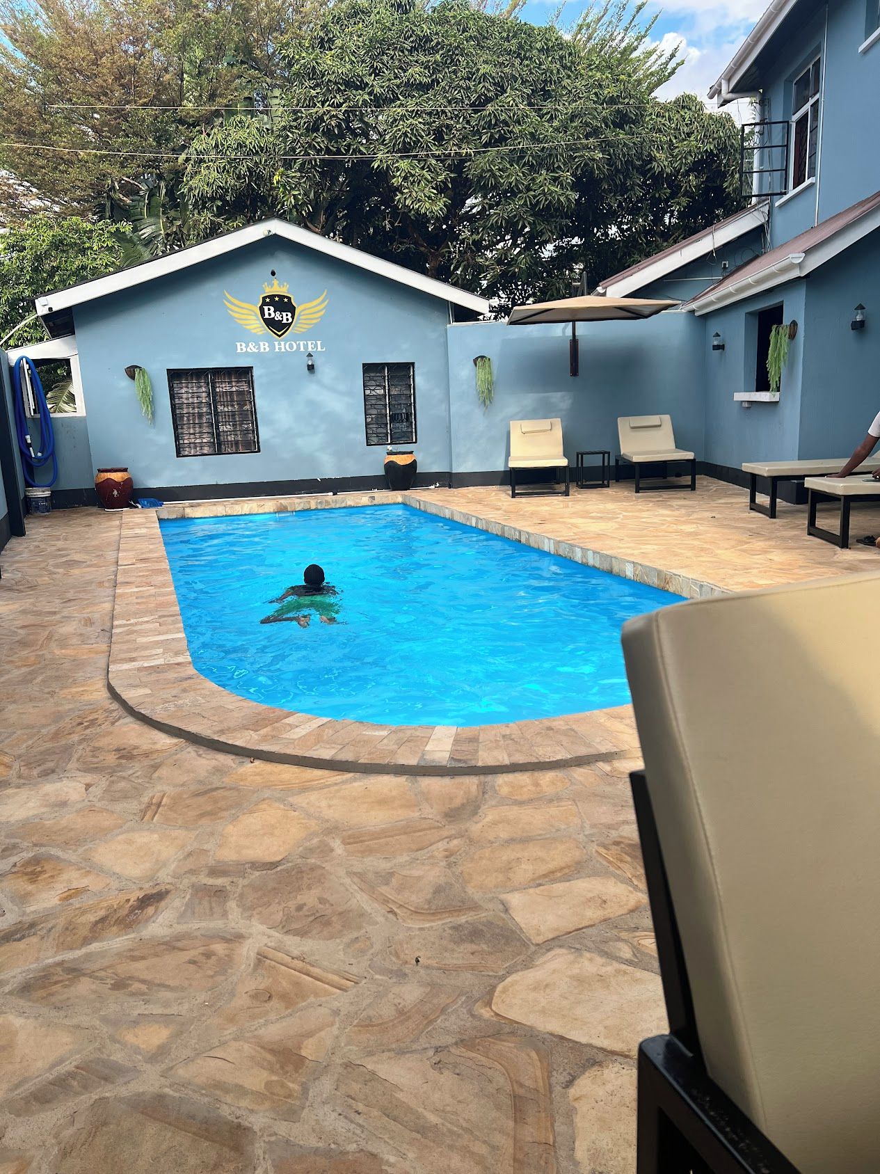 Zona de piscina con sillones de descanso y un edificio con el letrero 'B&B HOTEL' al fondo.