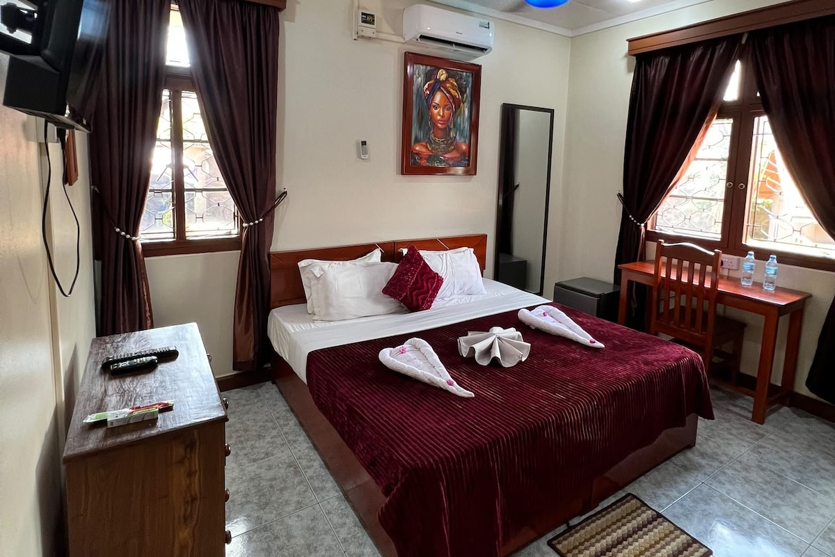 Una habitación de hotel con cama, escritorio, silla, televisor y aire acondicionado.