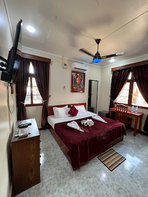 Una habitación de hotel con cama, escritorio, silla, televisor y aire acondicionado.