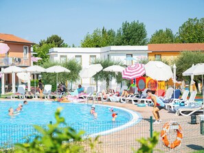 Ein Poolbereich mit Liegestühlen und Sonnenschirmen, umgeben von Gebäuden im mediterranen Baustil.