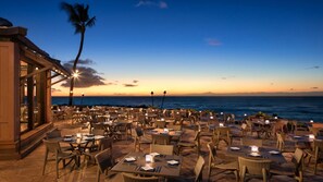 An outdoor dining area with tables and chairs, overlooking the ocean at sunset. - Ocean-View King at Ocean Tower – Waikoloa Beach Resort with Lanai (Waikoloa Village)