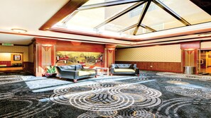Un hall d’hôtel doté d’un plafond haut, d’une verrière et d’un tapis à motifs.