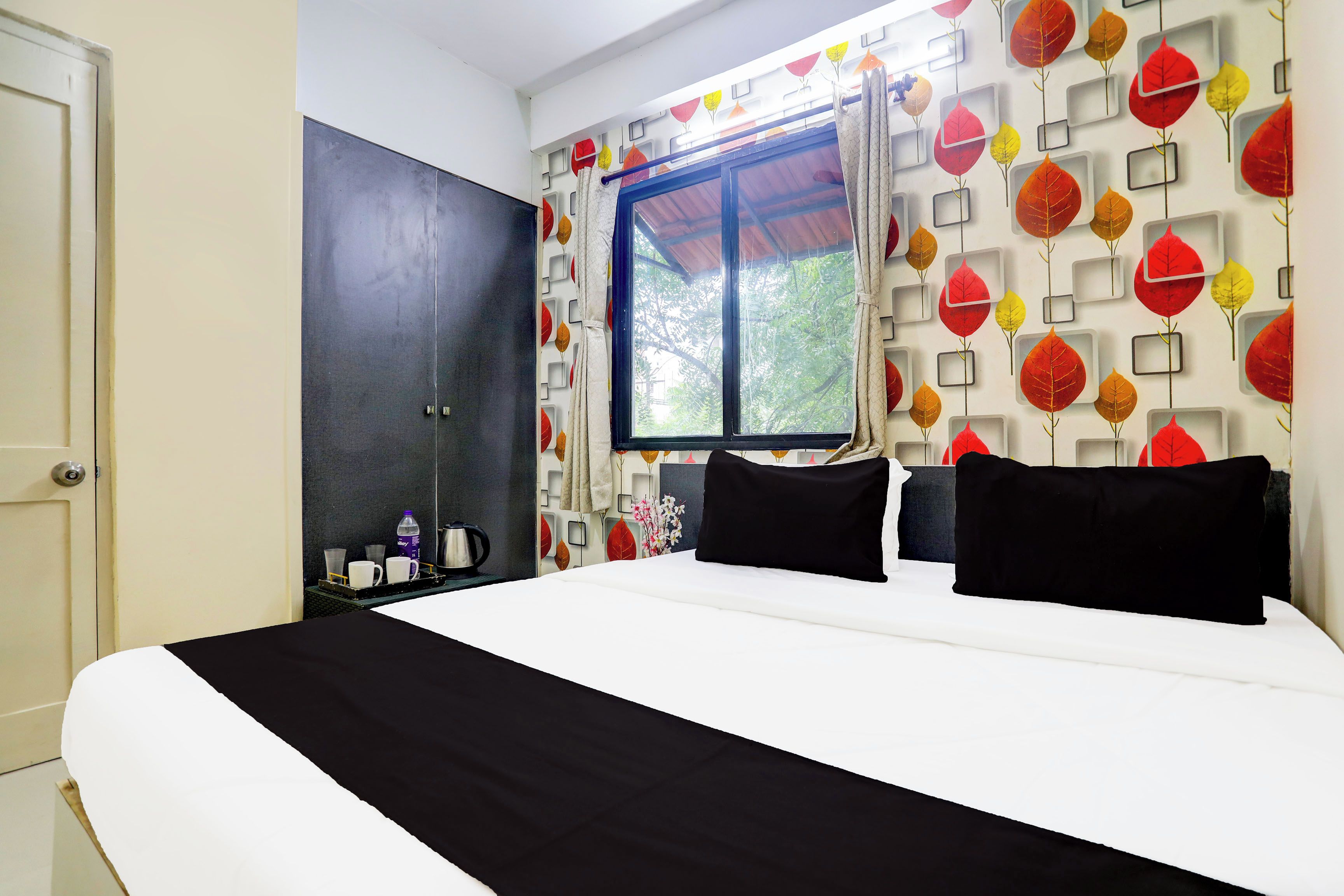 Un dormitorio con cama, armario, ventana y pared con motivos de hojas.