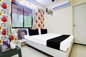 Habitación de hotel con cama, mesita de noche, ventana con cortinas, una pared con decoración de motivos de hojas y un equipo de aire acondicionado.