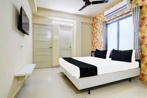Habitación de hotel con cama, televisor montado en la pared, ventilador de techo y aire acondicionado.