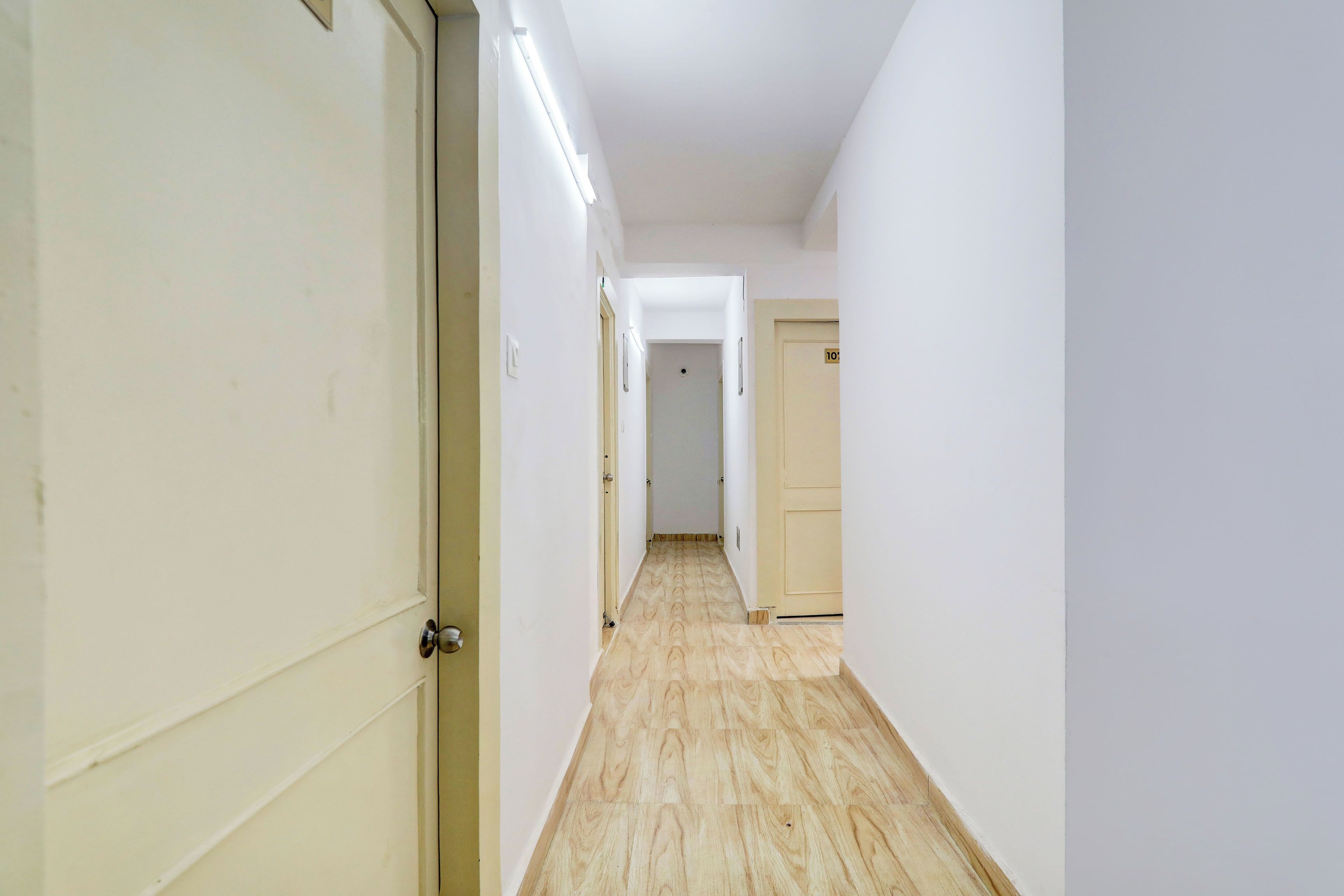 Un pasillo estrecho con suelo de madera, paredes blancas y puertas a ambos lados.