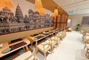 A restaurant with long tables and chairs, a mural of a temple, and hanging light fixtures. - Golden Bagh (Bhakhera)