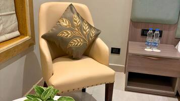 A modern armchair with a decorative pillow, a small table with a plant, and a wooden side table with water bottles and a plate.