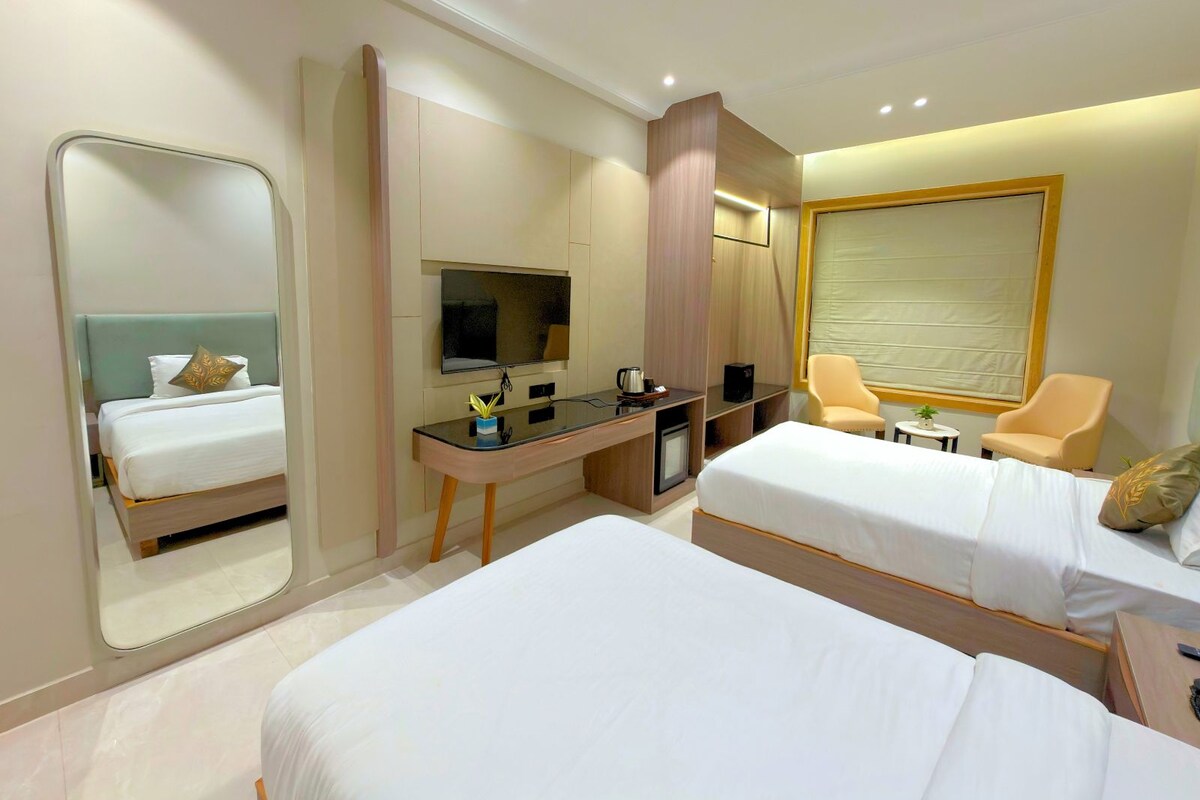 A hotel room with two beds, a desk with a flat-screen TV, a coffee maker, and a chair.