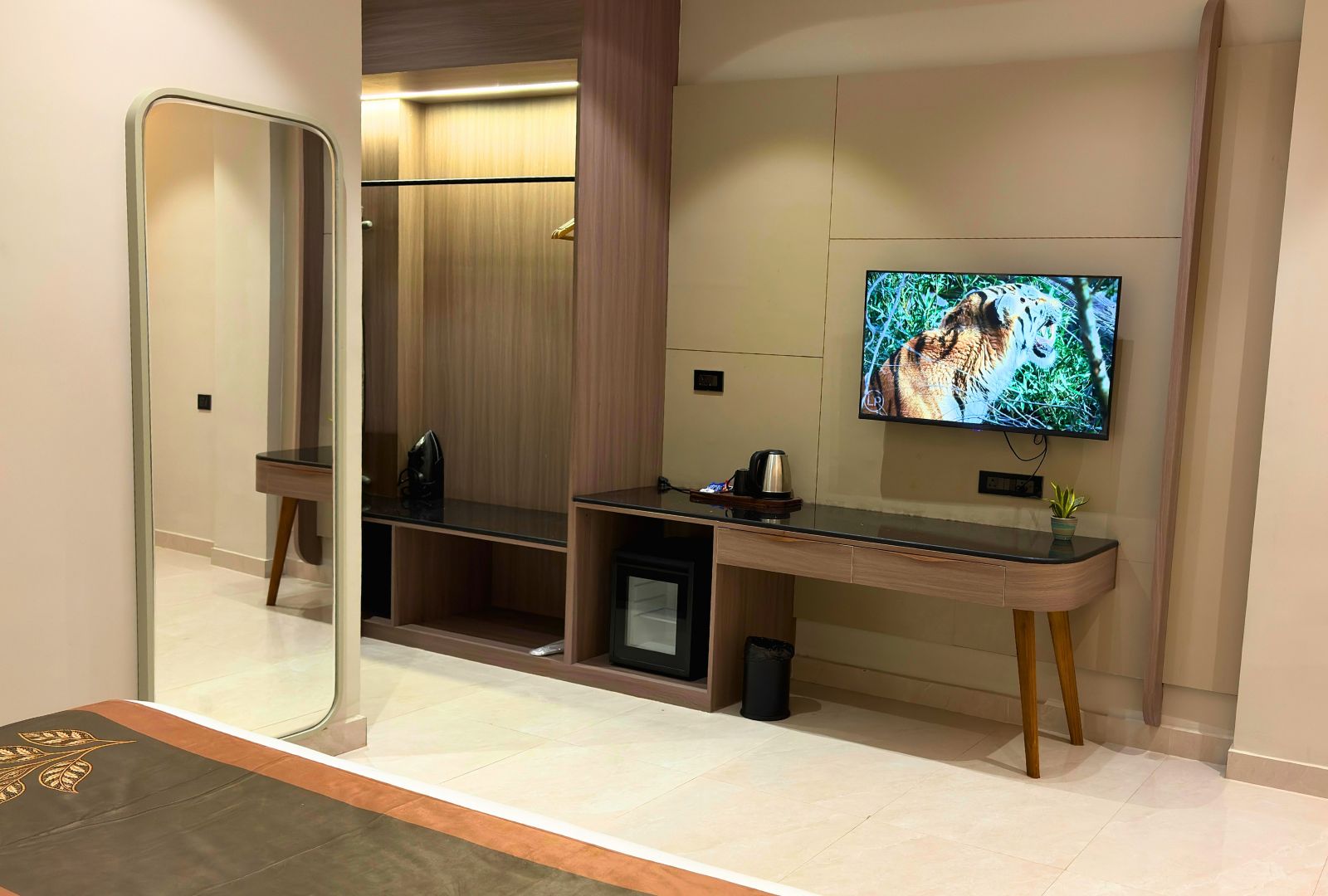 Une chambre d’hôtel dotée d’un grand miroir, d’un téléviseur à écran plat fixé au mur, d’un petit bureau avec une machine à café et d’un coin salon avec un banc.