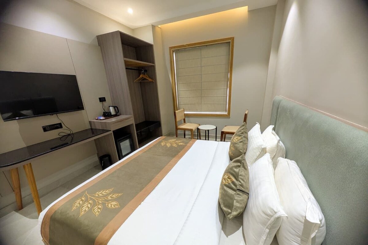 A hotel room with a bed, a desk, a TV, a window, and a seating area.