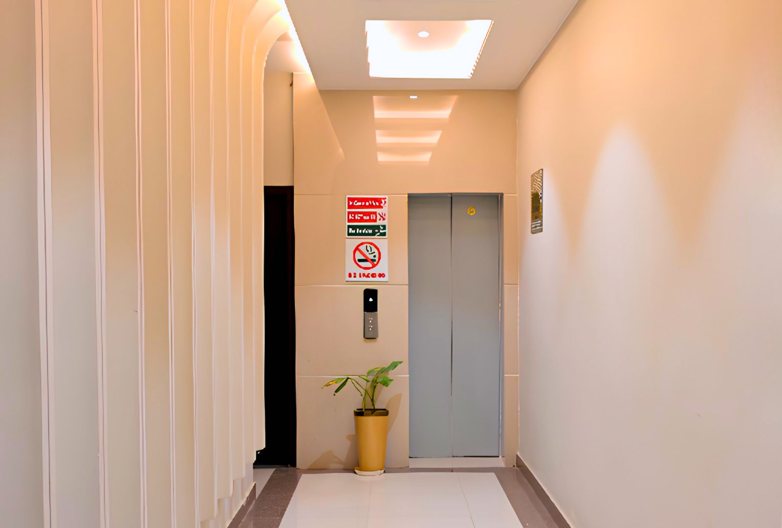 A hallway with a door, a no-smoking sign, and a potted plant.