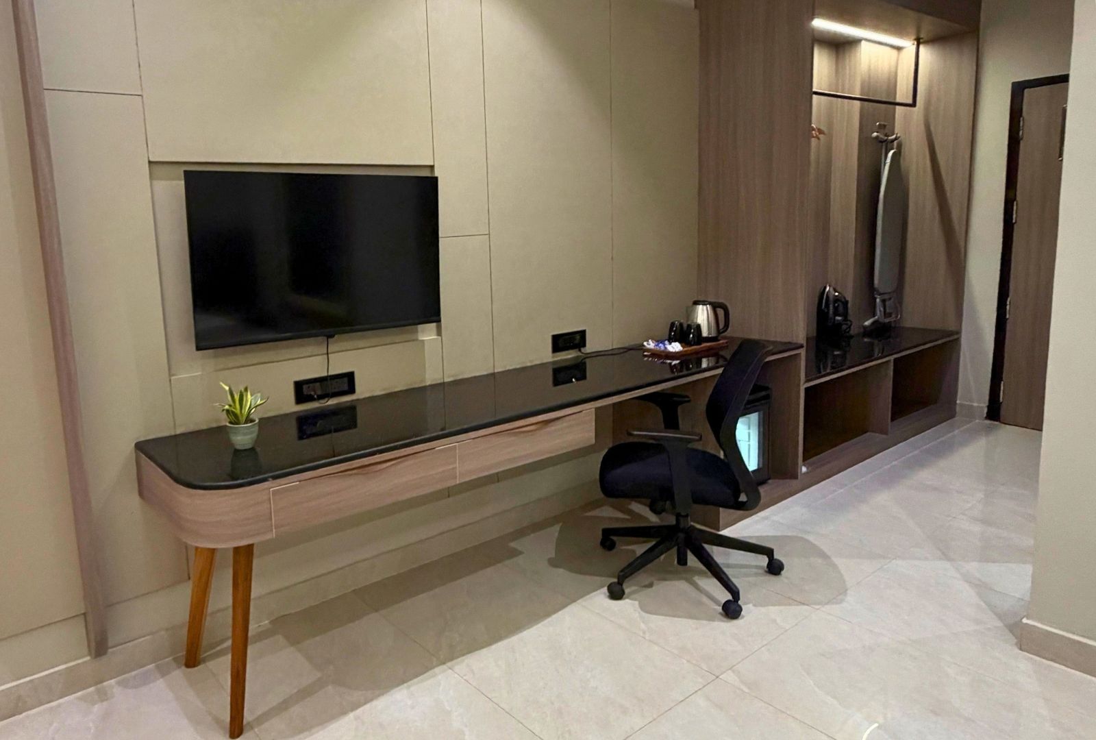 A modern office space with a long desk, a chair, a television mounted on the wall, and a coffee machine.
