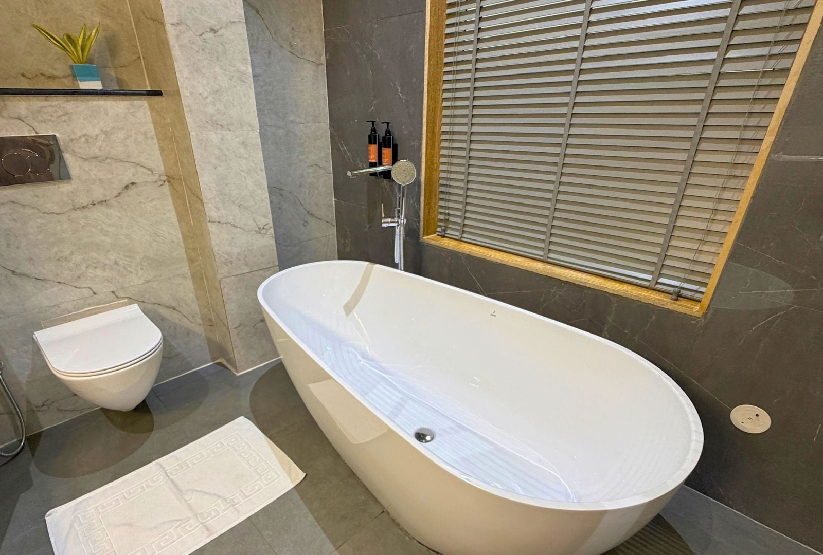 Une salle de bain moderne avec une baignoire sur pieds, des toilettes et une fenêtre avec des stores.