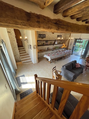 Un vaste espace de vie comprenant une table à manger pour quatre personnes, un canapé gris et un escalier menant à une chambre en mezzanine.