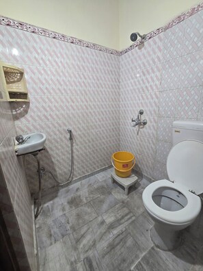 A bathroom with a toilet, sink, shower, and a yellow bucket on a small stool. - Sri Sai Guest House (Ranchi)