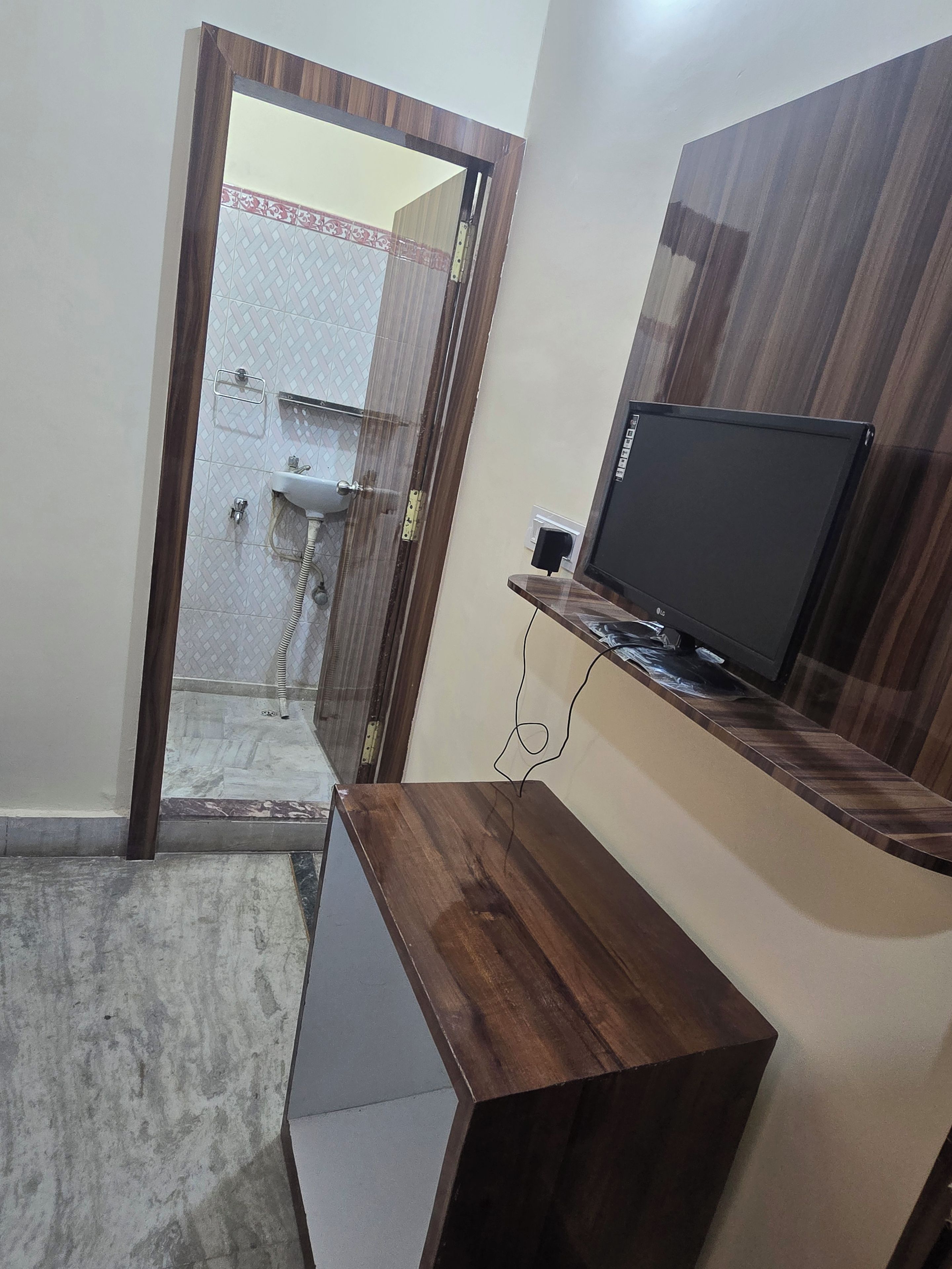 A bathroom with a shower, toilet, and a mirror. There is a wooden vanity with a television on top.