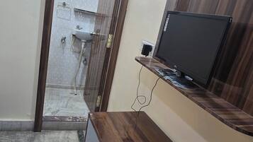 A bathroom with a shower, toilet, and a mirror. There is a wooden vanity with a television on top.