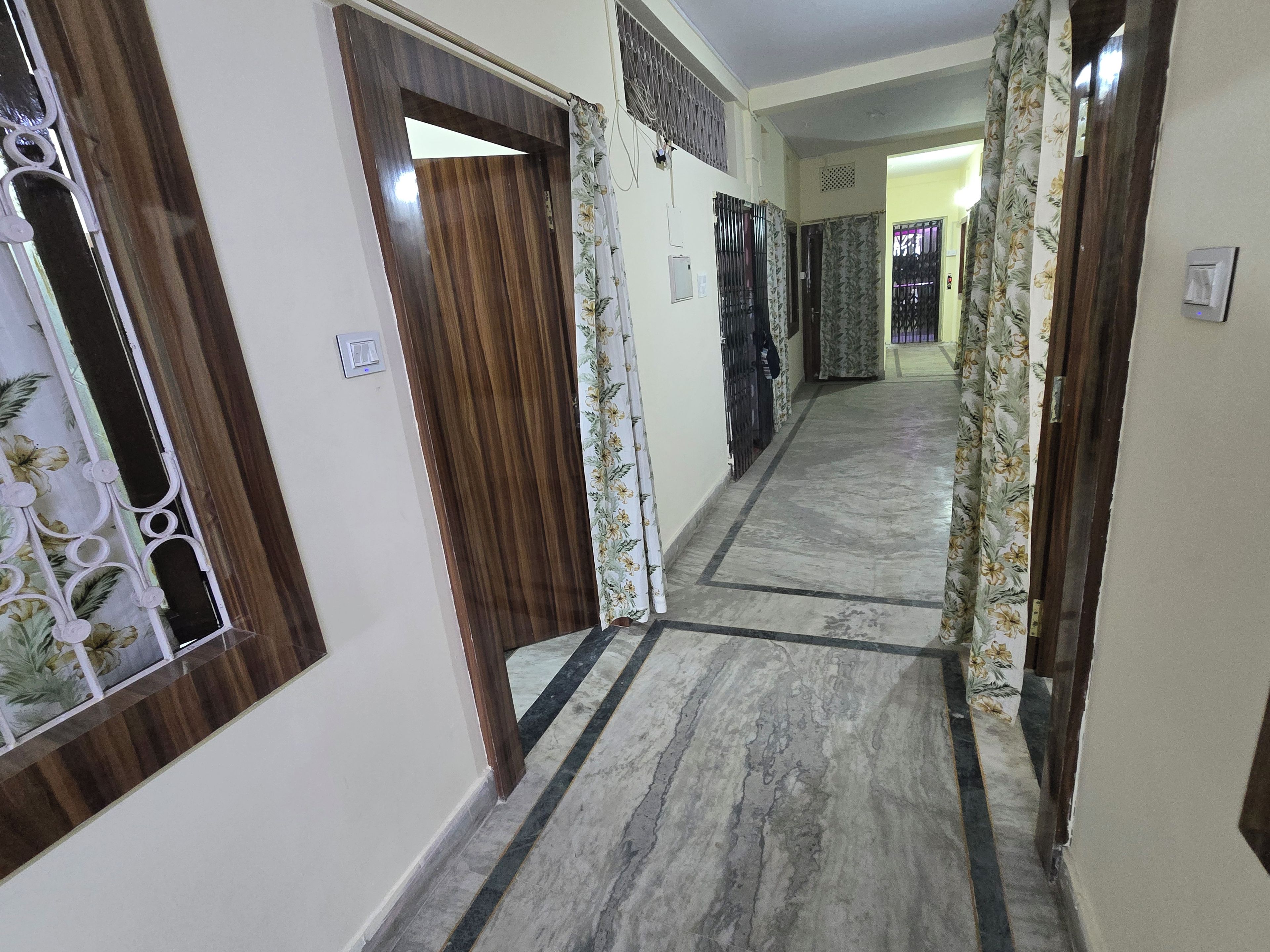 A hallway with a marble floor, wooden doors, and floral curtains.