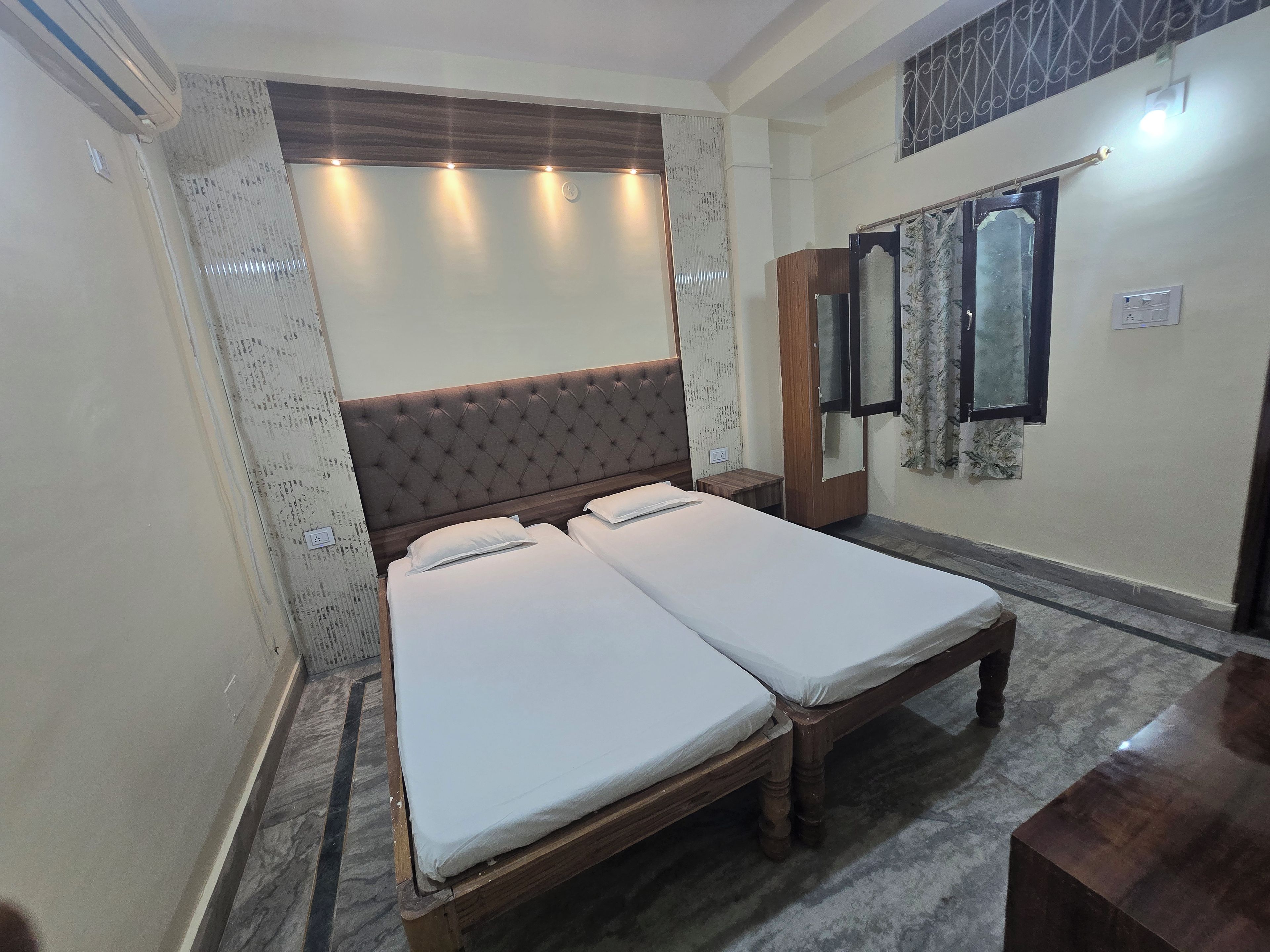A double bed with a wooden headboard, a bedside table, and a wardrobe in a room with a tiled floor.