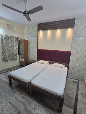 A double bed with a wooden frame and a red upholstered headboard, a ceiling fan, and a shower curtain with a floral pattern. - Sri Sai Guest House (Ranchi)