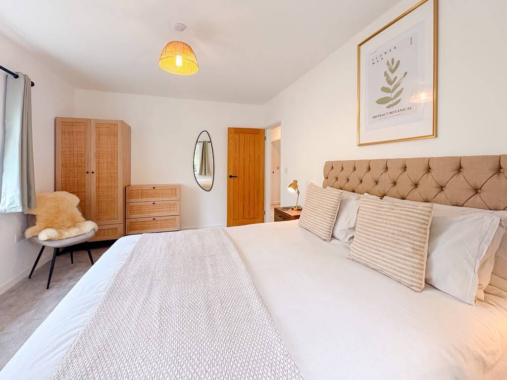 A bedroom with a large bed, a wardrobe, a mirror, and a framed botanical print on the wall.