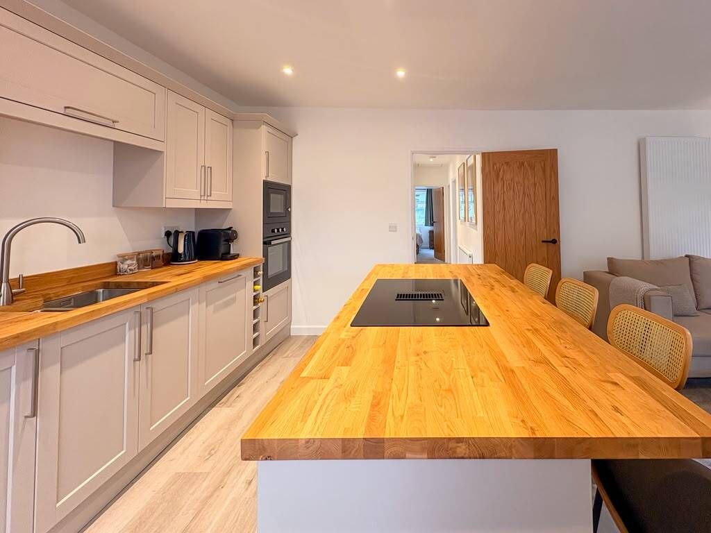 A modern kitchen with white cabinetry, a wooden island, and a built-in oven.