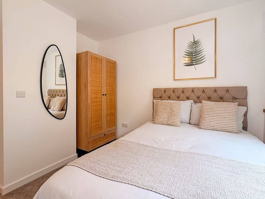 Una camera da letto con un letto, un armadio, uno specchio e un’opera d’arte con foglie in cornice appesa al muro.