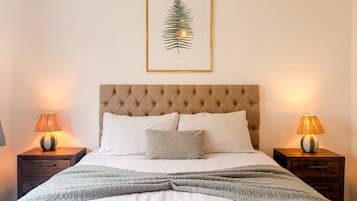 A neatly made bed with a tufted headboard, two bedside lamps, and a framed leaf artwork above.