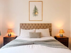 A neatly made bed with a tufted headboard, two bedside lamps, and a framed leaf artwork above.