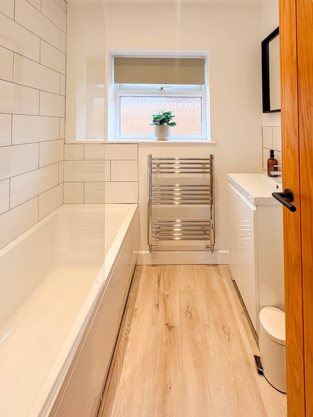 A narrow bathroom with a bathtub, a towel rack, a window with a plant, and a toilet.