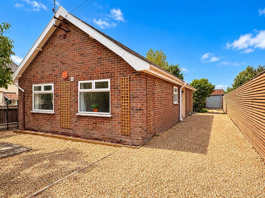 A single-story brick house with a gabled roof, a small front porch, and a gravel driveway.