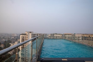 A rooftop swimming pool with a glass barrier, surrounded by buildings. - The Cozy House 1BHK Near BKC (Mumbai)
