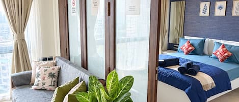A hotel room with a sofa, a bed with blue bedding, a potted plant, and a sliding door with a sign indicating free WiFi.