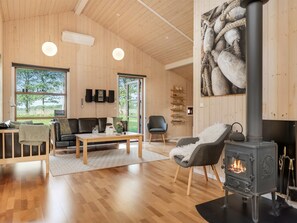 A cozy living room with a fireplace, wooden walls, and a large window overlooking a garden. - "Torsten" by Interhome (Ejstrupholm)