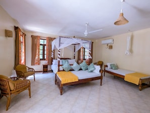 A room with a four-poster bed, two single beds, wicker furniture, and a ceiling fan. - 4-bedroom Beach Villa in superb Diani Beach with Private Pool & spectacular view (Diani Beach)