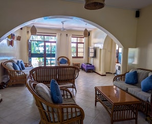 A spacious living area with wicker furniture, a ceiling fan, and large windows allowing natural light. - 4-bedroom Beach Villa in superb Diani Beach with Private Pool & spectacular view (Diani Beach)