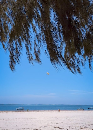 A beach with a clear sky, a boat on the water, and people walking on the sand. - 4-bedroom Beach Villa in superb Diani Beach with Private Pool & spectacular view (Diani Beach)