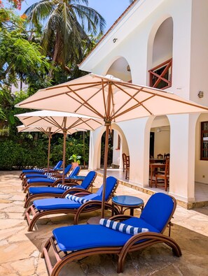 A row of sun loungers with umbrellas, a stone patio, and a building with arches. - 4-bedroom Beach Villa in superb Diani Beach with Private Pool & spectacular view (Diani Beach)