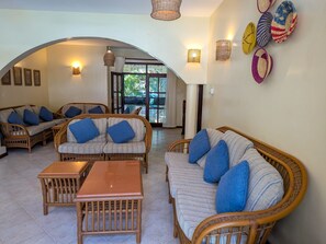 A spacious lounge area with wicker furniture, a wooden coffee table, and a view through an arched doorway to an outdoor area. - 4-bedroom Beach Villa in superb Diani Beach with Private Pool & spectacular view (Diani Beach)