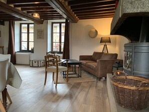 Ein gemütliches Wohnzimmer mit einer Couch, einem Tisch, einem Sessel, einem Kamin und einem Fenster mit Vorhängen.